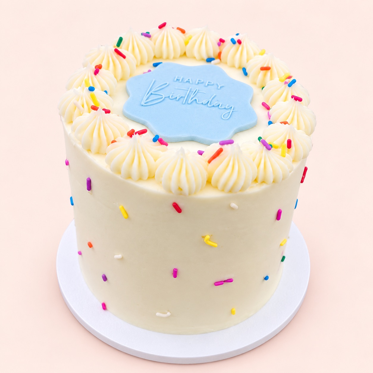 Small white bento cake with rainbow sprinkles, piped buttercream swirls and a blue “Happy Birthday” plaque