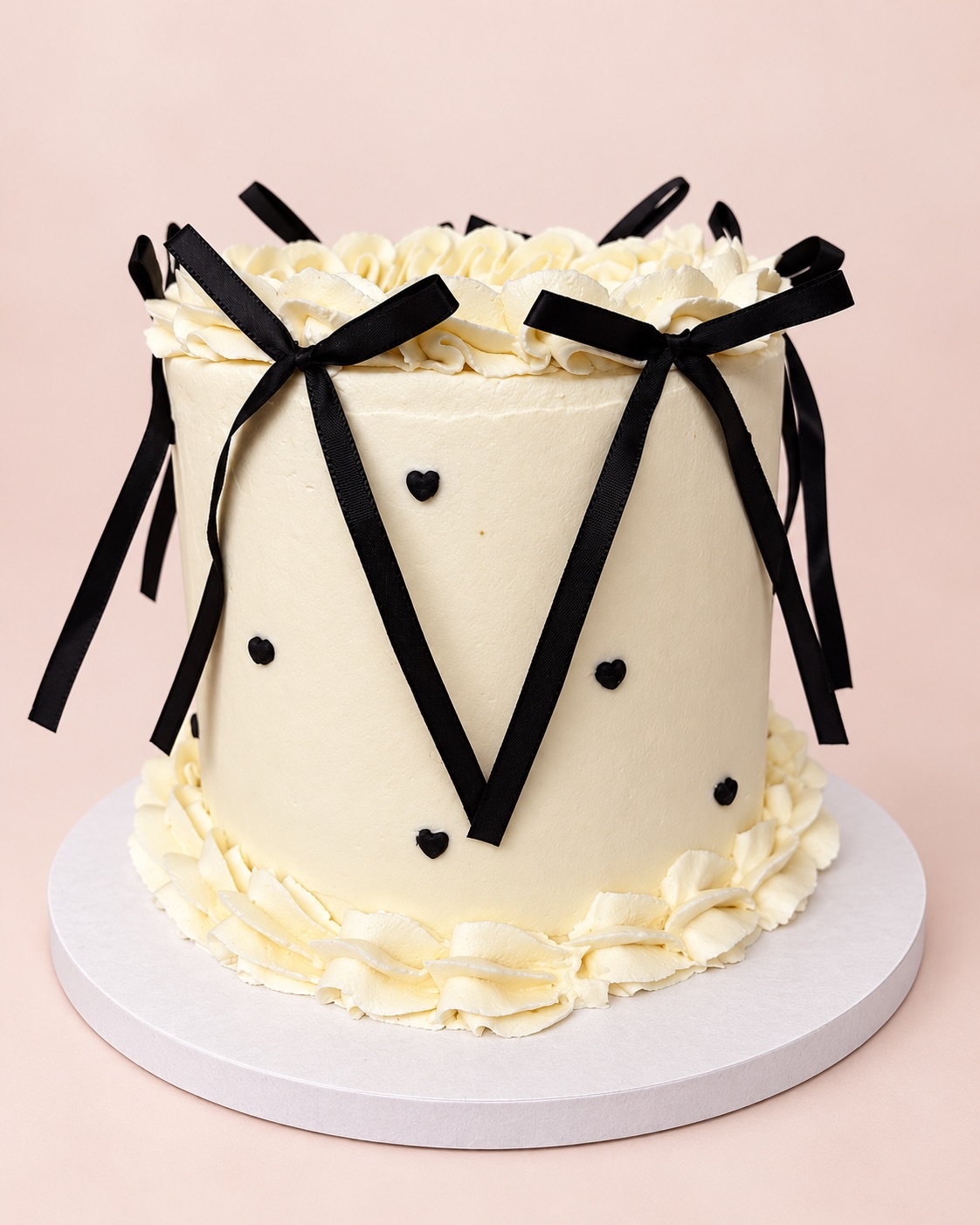 Tall cream buttercream celebration cake with piped borders, tiny black hearts and black ribbon bows