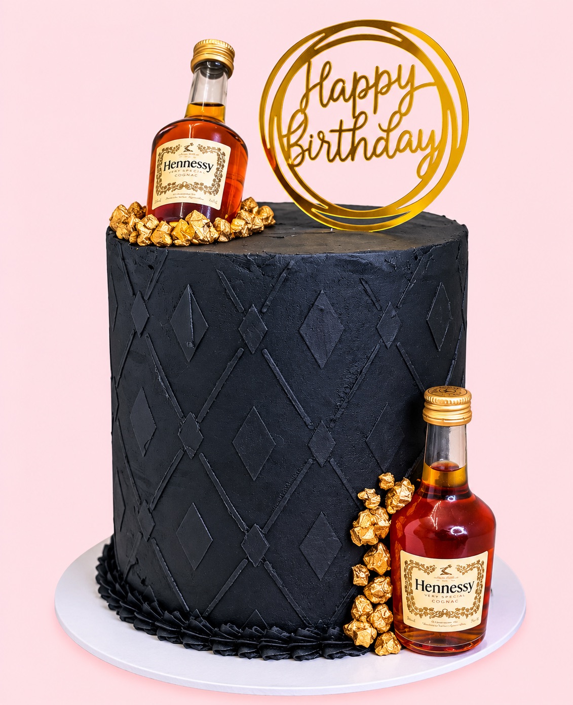Tall black buttercream cake with a diamond pattern, gold nuggets, two mini bottles and a gold Happy Birthday topper