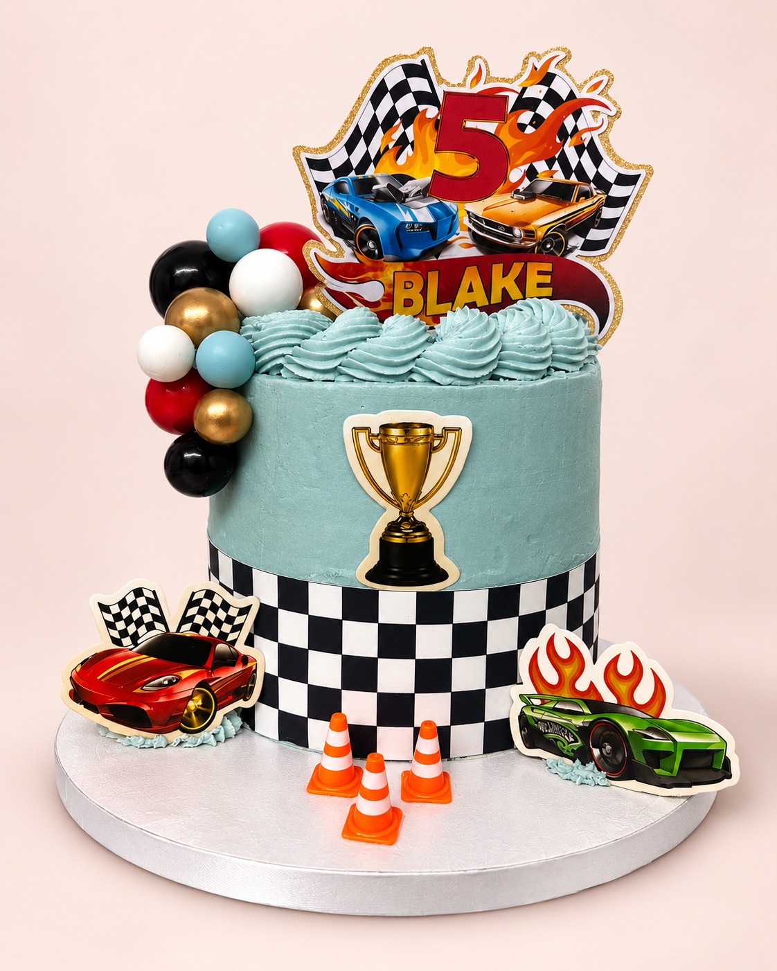 Pale blue racing car cake with a chequered band, toy cars, traffic cones and a “Blake 5” topper